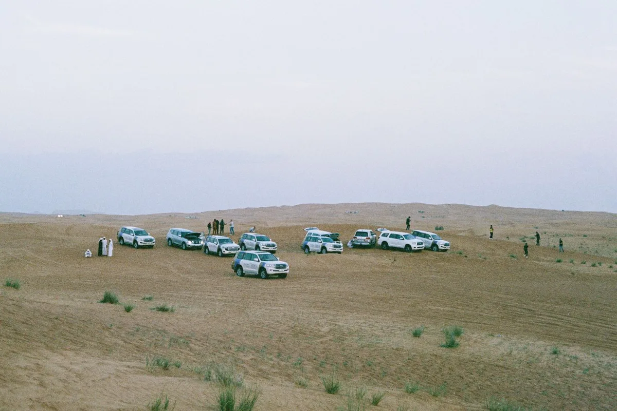 White four-wheel-drive vehicles travelling across desert dunes
